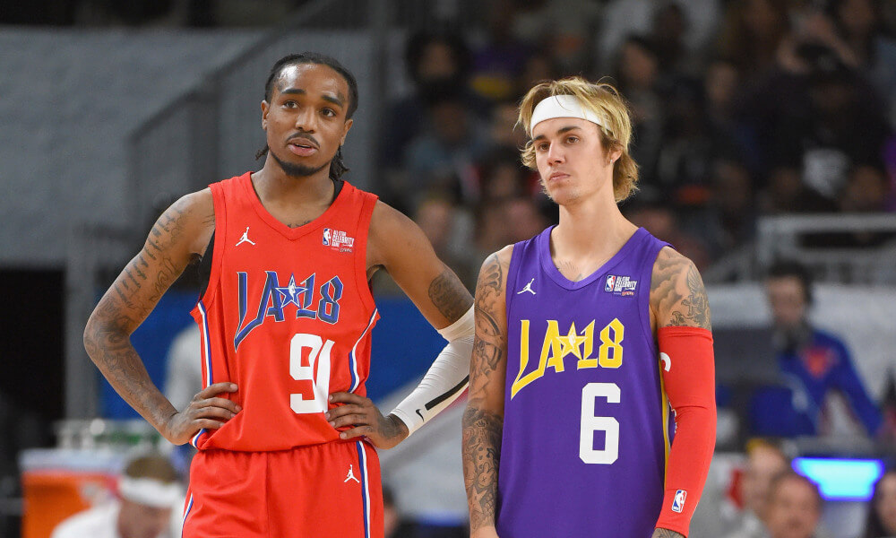 Quavo dan Justin Bieber mengenakan jersey berwarna orange dan ungu saat mengikuti pertandingan basket